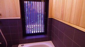A bathroom with a window, a bathtub, and wooden cabinetry.