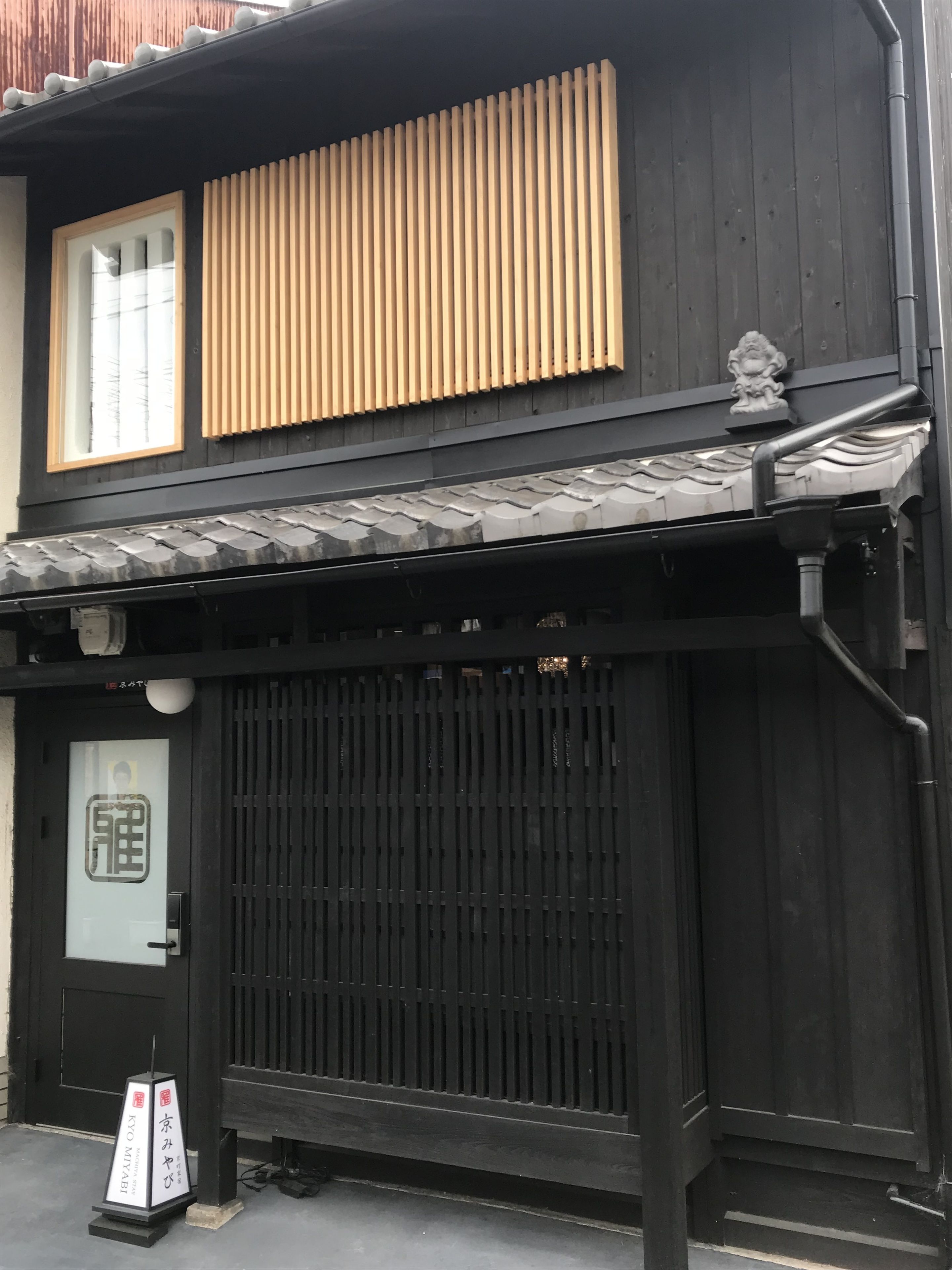 A traditional Japanese building with a black exterior, a sliding wooden door, and a small signboard outside.