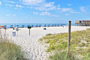 A beach with umbrellas and beach chairs, a wooden structure, and a sign on the sand.