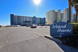 A parking lot with a sign for 'Island Shores' and a building in the background.