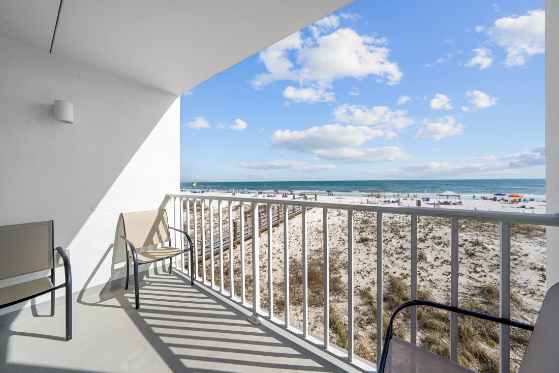 En balkon med udsigt over en strand, med gelænder og et par stole.