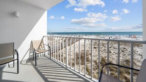 Un balcon donnant sur une plage, avec une balustrade et quelques chaises.