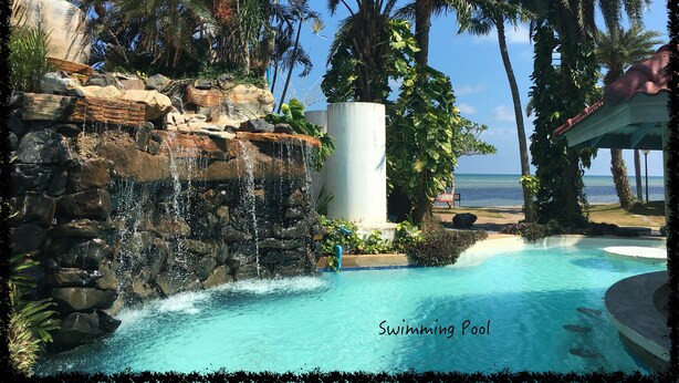 A swimming pool with a waterfall feature, surrounded by palm trees and a view of the ocean. - 3 bdrm, 3 ba home with 24 hr security in private Villa. Located nr beach & pools (Kram)