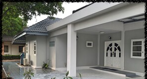 Uma casa com um pátio cerâmico novo, um alpendre coberto e uma porta com painéis de vidro decorativos.