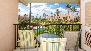 Un balcón con dos sillas a rayas y una mesa, con vistas a una piscina y palmeras.