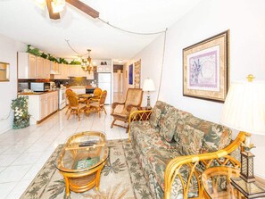 A spacious living room with a sofa, chairs, and a coffee table. There is a kitchen area with cabinets and a dining table.