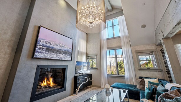 A spacious living room with a fireplace, large windows, and a chandelier.