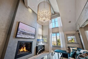 A spacious living room with a fireplace, large windows, and a chandelier. - Silver Star 41DX | Near Silver Star Lift (Park City)