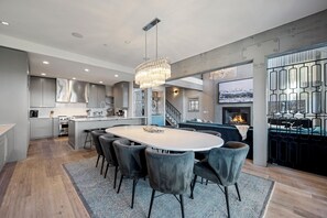 A modern kitchen with a central island, a dining area with chairs, and a staircase leading to an upper level.
