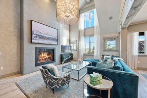 A spacious living room with a fireplace, a large window, and a chandelier.