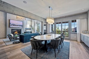 A modern kitchen with a large island, dining table, and chairs, a fireplace, and large windows with a view.