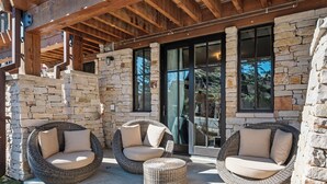 A stone exterior with a covered patio area featuring wicker chairs and a small ottoman.