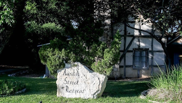 Une pancarte en pierre portant l’inscription « Austin Street Retreat », placée devant un bâtiment au style architectural traditionnel.