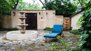 Une cour pavée de pierres avec une fontaine, un fauteuil de jardin bleu et une porte en bois.