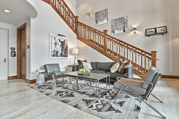 A spacious living room with a high wooden staircase, a large abstract painting, and a modern sofa set.