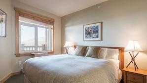 Un dormitorio ordenado con una cama grande, dos lámparas de noche, una ventana con persianas y un cuadro en la pared.