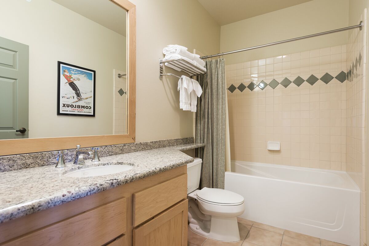 A bathroom with a granite countertop sink, a toilet, and a bathtub.