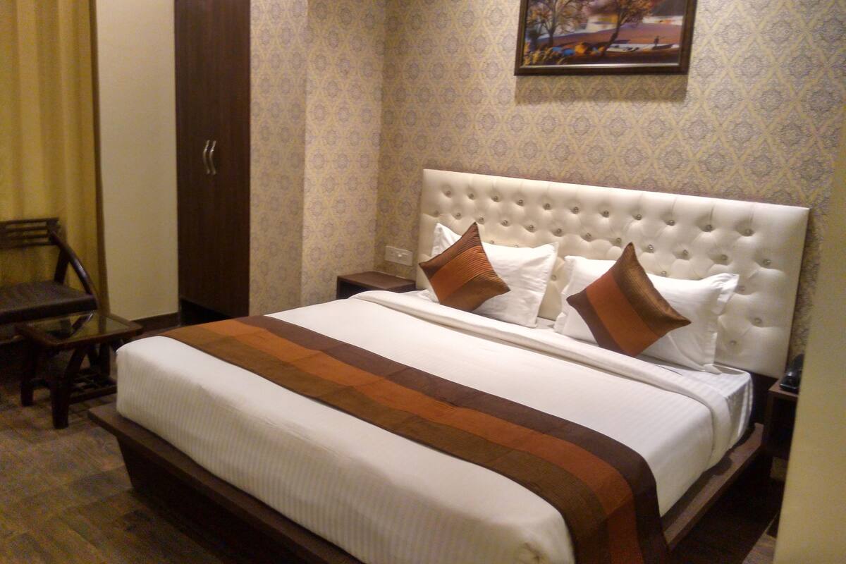 A neatly made bed with a tufted headboard, a wooden nightstand, and a wardrobe.