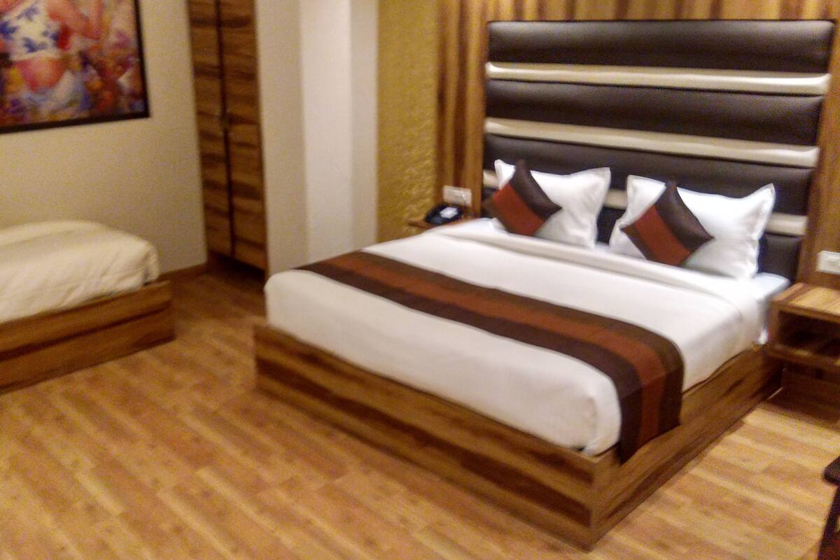 A hotel room with two beds, wooden flooring, a large painting on the wall, and a modern headboard.