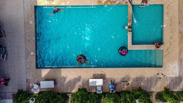 En vy från ovan av en rektangulär swimmingpool med två separata avsnitt, omgiven av solstolar och en liten uteplats.
