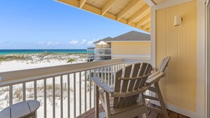Un balcon avec vue sur la plage, une chaise en bois et une petite table.