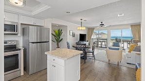 Une cuisine moderne équipée d’appareils électroménagers en acier inoxydable, un coin repas offrant une vue sur l’océan et un salon confortable avec un balcon donnant sur la mer.
