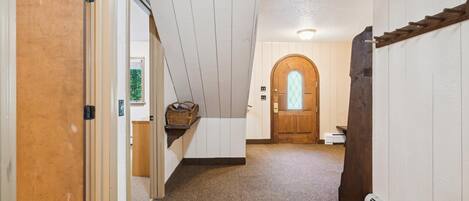 A hallway with a wooden door on the left, a white wall with a window, and a wooden door at the end.