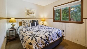 A bedroom with a bed, two bedside lamps, a ceiling fan, a framed picture, and a window with a view of trees. - Cozy 4-Bedroom Townhouse– Ideal for Groups & Families Snow Flake (Killington)