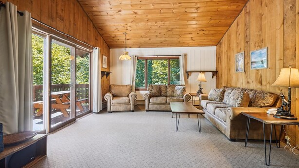A cozy cabin interior with a wooden ceiling, a sofa, a chair, a coffee table, and a dining table. - Cozy 4-Bedroom Townhouse– Ideal for Groups & Families Snow Flake (Killington)