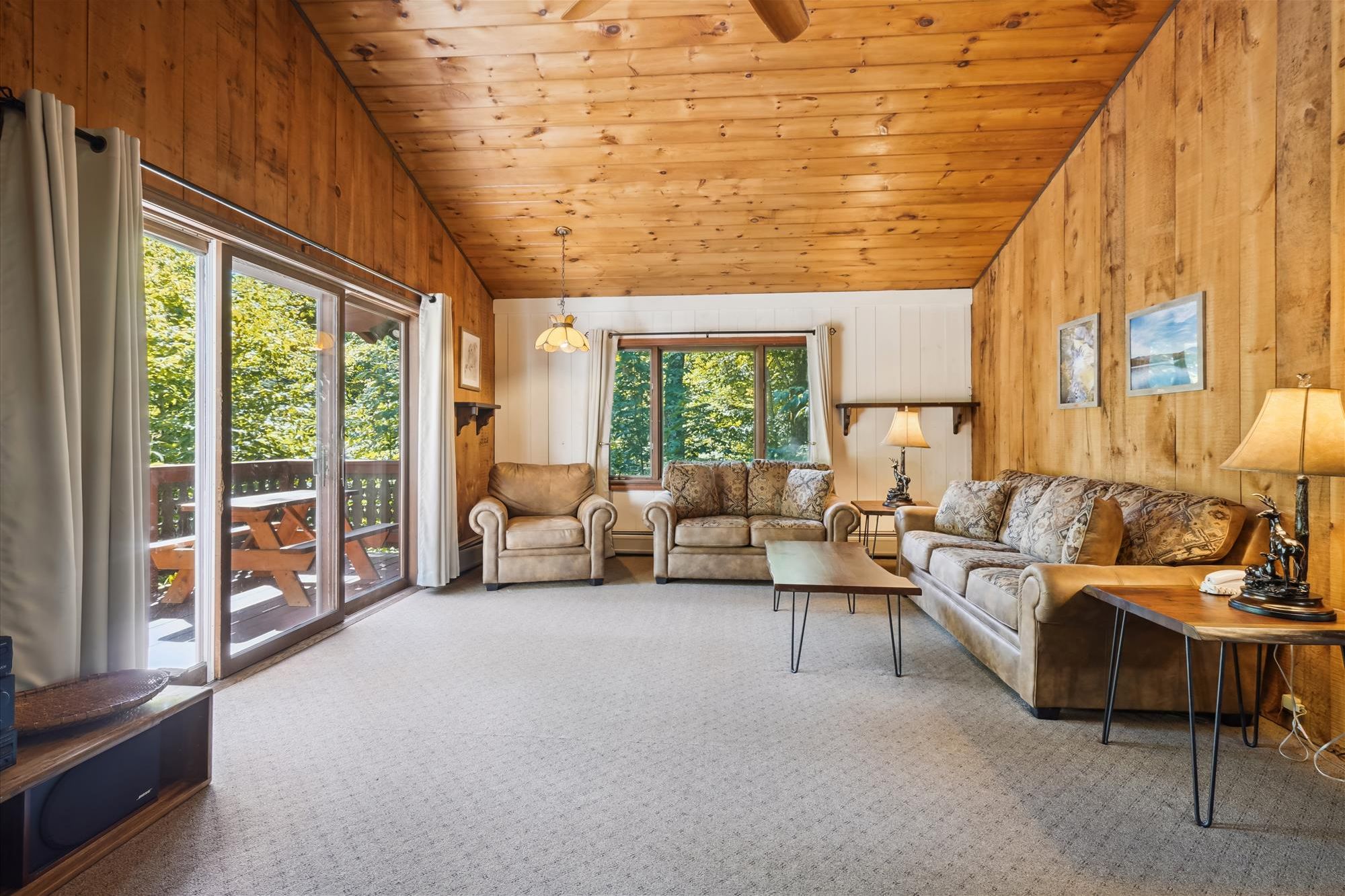 L’intérieur d’un chalet accueillant, avec un plafond en bois, un canapé, un fauteuil, une table basse et une table à manger.