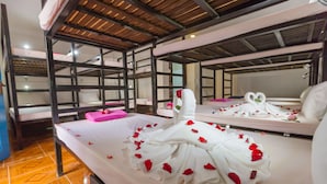 Une chambre d’hôtel avec des lits superposés, un lit parsemé de pétales de rose et un miroir qui reflète la pièce.