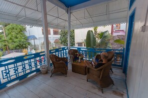 A covered outdoor seating area with wicker furniture and a blue railing. - Kafu Hostel & Pool (Siem Reap)