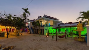Une propriété située en bord de mer, comprenant une grande maison, un petit sanctuaire et un espace repas avec des sièges à l’extérieur.