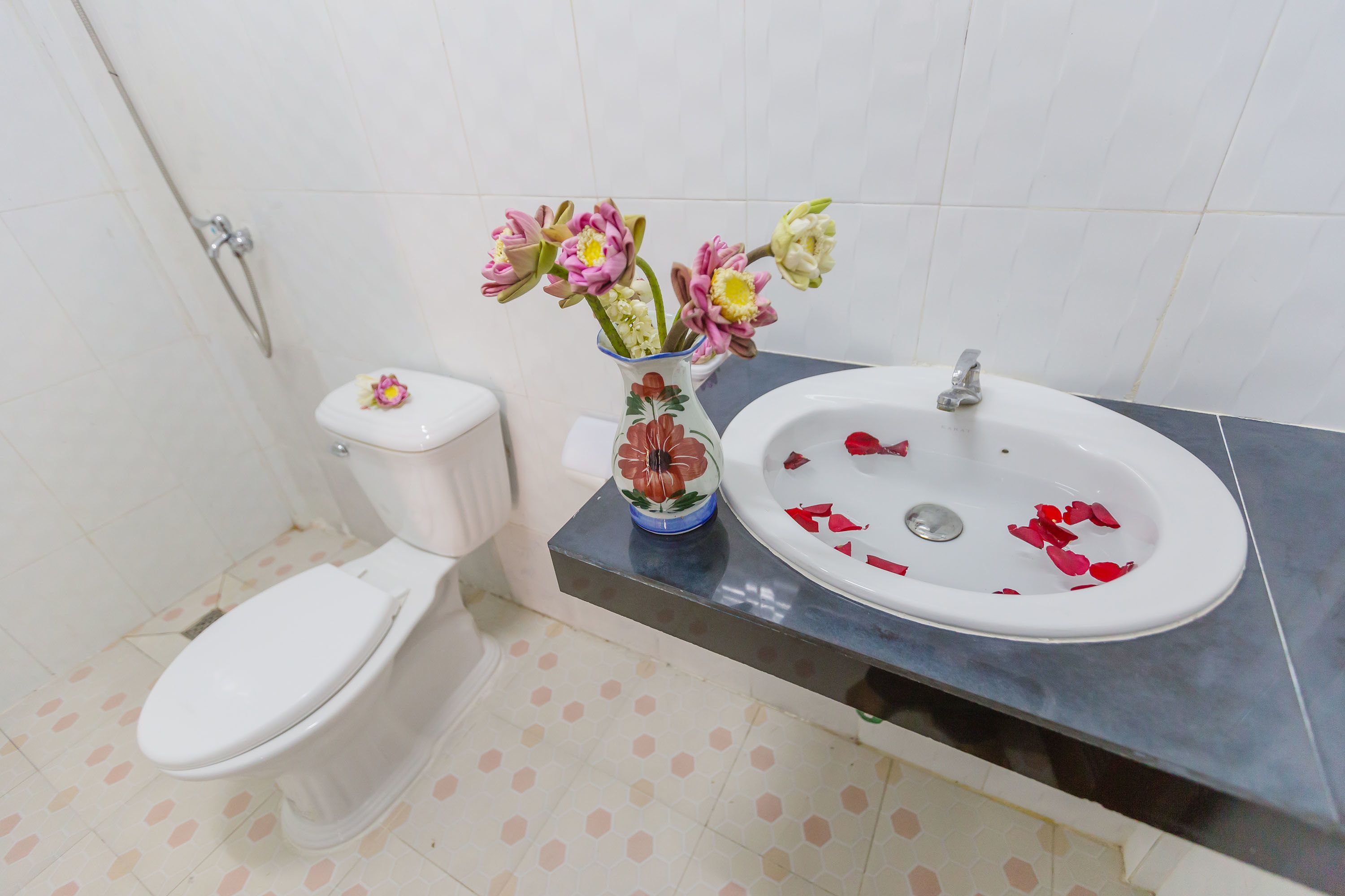 Une salle de bain avec des toilettes, un lavabo décoré de pétales de rose et un vase rempli de fleurs.