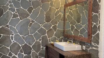 Une salle de bain avec un mur en pierre, un meuble-lavabo en bois et un miroir.