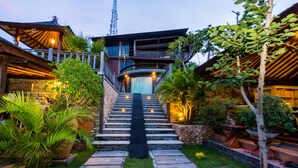 A staircase leading to a building with a balcony, surrounded by potted plants and a stone pathway. - Jenggala Hill (Lembongan Island)