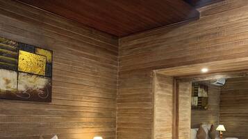 Una habitación de hotel con pared de madera, una cama con ropa de cama blanca, una mesita de noche con lámpara y un espejo.