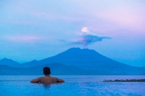 Eine Person in einem Schwimmbecken, im Hintergrund ein Berg und ein Vulkan.