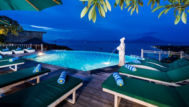 A poolside area with lounge chairs and a statue. - Jenggala Hill (Lembongan Island)