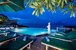 A poolside area with lounge chairs and a statue. - Jenggala Hill (Lembongan Island)