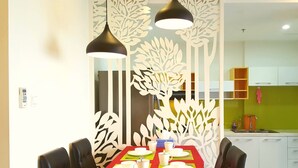 A dining area with a table set for four, two black pendant lights, and a decorative white partition with leaf patterns. - Sunrise City 2BR Luxury SWPool 30th (Ho Chi Minh City)