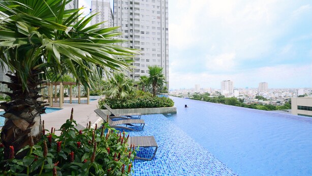 A rooftop infinity pool with a city view, surrounded by greenery and modern buildings. - Sunrise City 2BR Luxury SWPool 30th (Ho Chi Minh City)