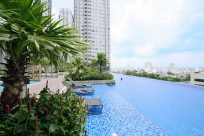A rooftop infinity pool with a city view, surrounded by greenery and modern buildings. - Sunrise City 2BR Luxury SWPool 30th (Ho Chi Minh City)