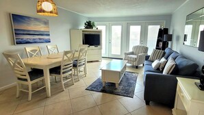 A modern living room with a dining area, a sofa, a TV, and a lamp. - Golf-Side 1BR Resort Amenities & Beach Access (Destin)