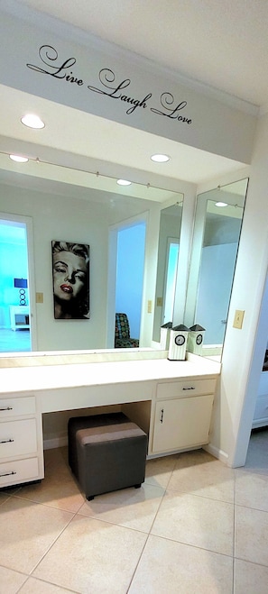 A bathroom with a large mirror, a vanity with drawers, a small stool, and a wall with a 'Live Laugh Love' sign. - Golf-Side 1BR Resort Amenities & Beach Access (Destin)