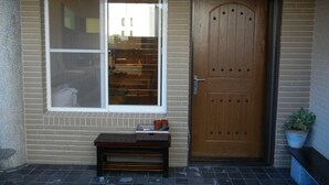 Une porte en bois avec une fenêtre au-dessus, un banc devant et un pot de fleurs sur la droite.