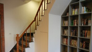 Un escalier avec des balustrades en bois menant à un palier, une bibliothèque remplie de livres et un mur sobre avec une porte.