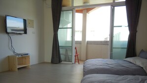 Une chambre à coucher avec un lit, un téléviseur fixé au mur, une étagère en bois et un balcon avec une chaise.