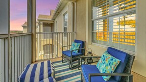 Un balcon avec deux fauteuils bleus dotés de coussins, un tapis à rayures et une petite table sur laquelle est posée une lanterne.