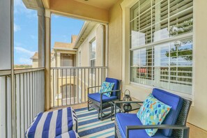 A balcony with two chairs and a table, a striped rug, and a view of a house through the railing.